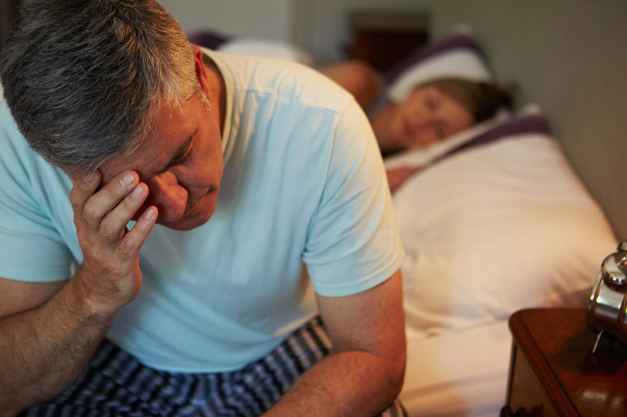Man die zijn voorhoofd vasthoudt terwijl hij op de rand van zijn bed zit